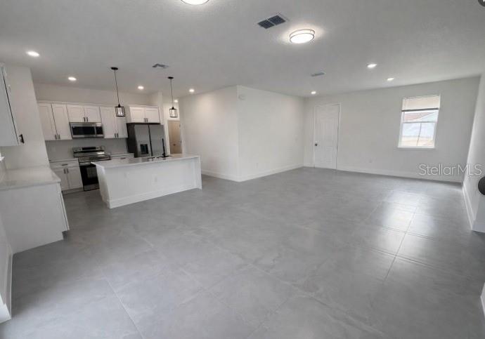 A modern kitchen with white cabinets and a center island opens into a spacious living area — 4837 SW 138TH LANE, OCALA, FL