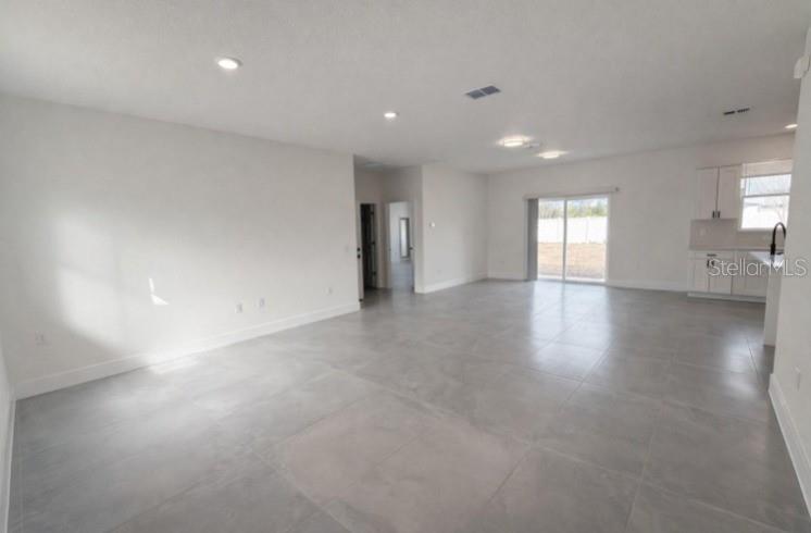 An open-concept living area features light gray tile flooring, white walls, and a modern kitchen — 4837 SW 138TH LANE, OCALA, FL