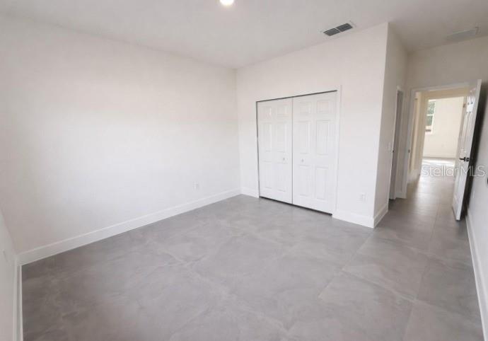 A bedroom with white walls, gray tile flooring, and a white double-door closet — 4837 SW 138TH LANE, OCALA, FL