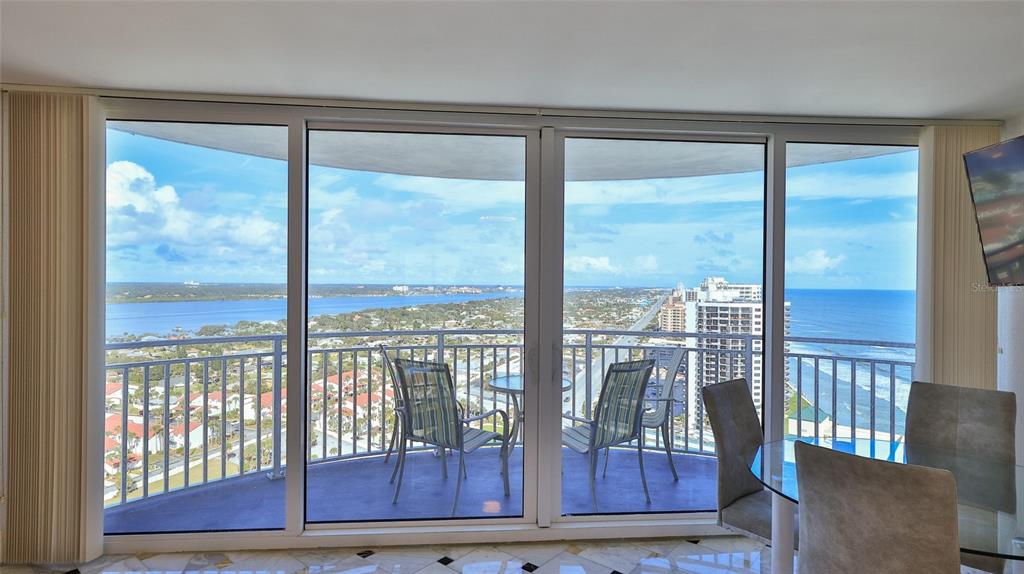 A dining area with a glass table overlooks a balcony and a coastal city view — 2625 S ATLANTIC AVENUE UNIT 24NW, DAYTONA BEACH, FL