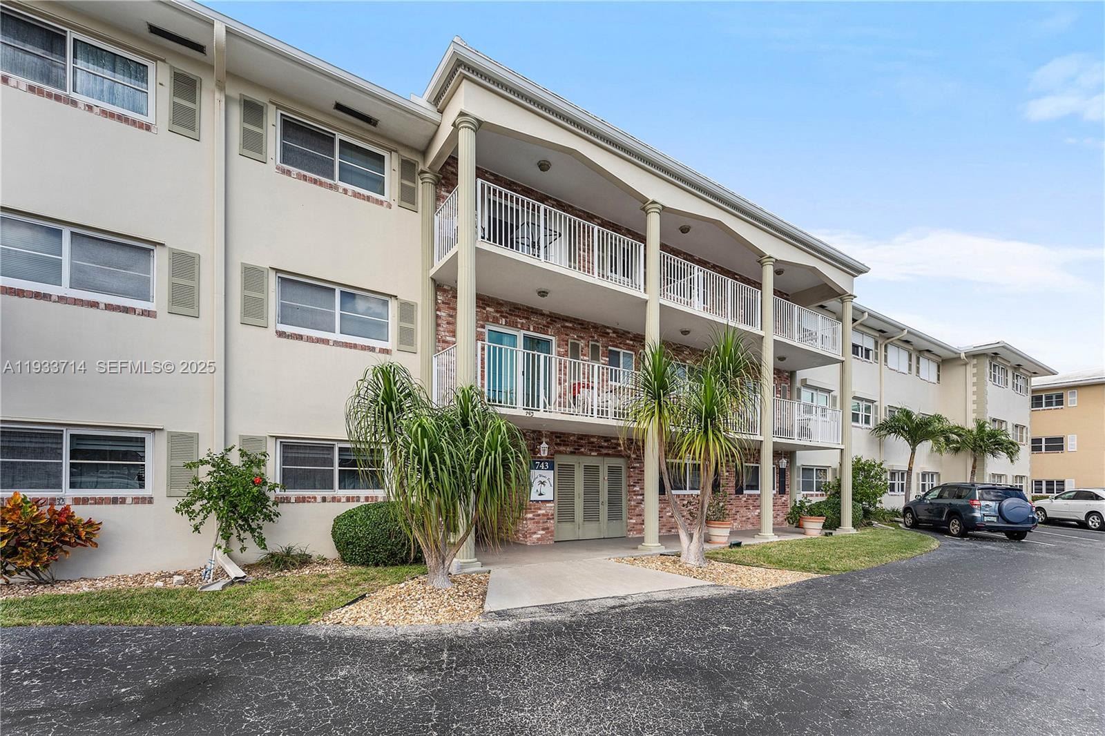 A three-story apartment building features a brick facade, white balconies, and a paved parking lot — 743 N Riverside Dr # 5C, Pompano Beach FL 33062, POMPANO BEACH, FL