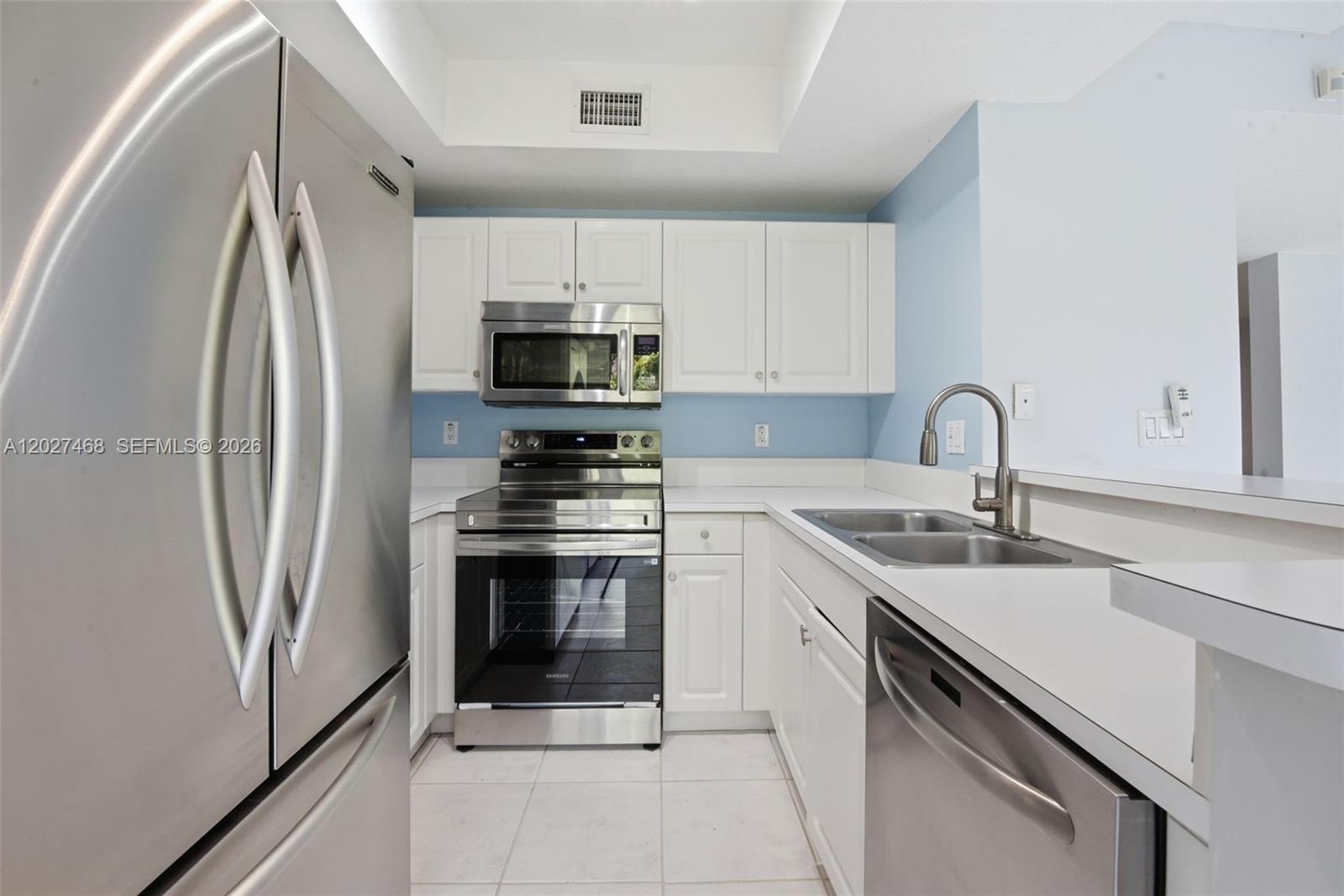 A kitchen features white cabinets, stainless steel appliances, a double sink, and light-colored tile flooring — 10180 SW 88th St # 403, Miami FL 33176, MIAMI, FL