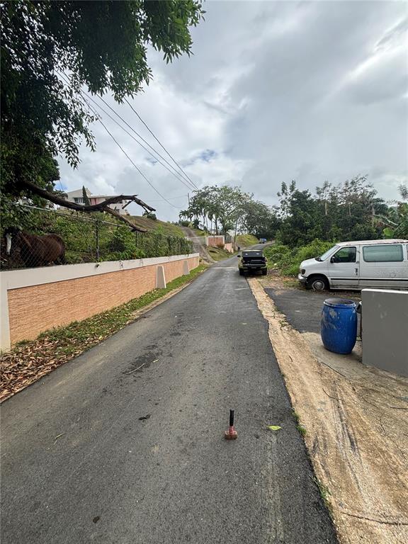 A narrow paved road leads uphill past a retaining wall, a parked van, and trees — RD 842 KM 4.6 INT, SAN JUAN, PR