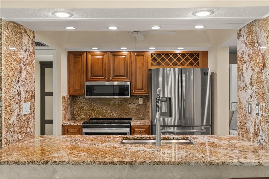 A kitchen features wood cabinets, stainless steel appliances, and granite countertops with a breakfast bar — 450 S GULFVIEW BOULEVARD UNIT 802, CLEARWATER BEACH, FL