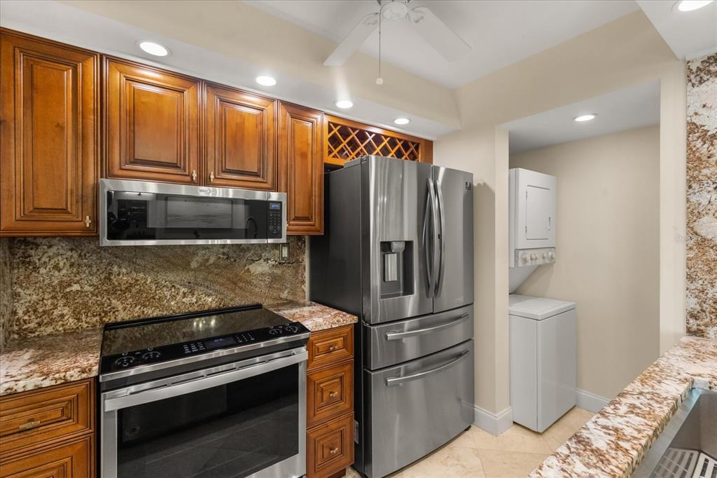 A kitchen features wood cabinets, granite countertops, stainless steel appliances, and an adjacent laundry area — 450 S GULFVIEW BOULEVARD UNIT 802, CLEARWATER BEACH, FL
