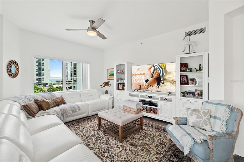 A living room features a white sectional sofa, a television, and a view of buildings — 2 OCEANS WEST BOULEVARD UNIT 606, DAYTONA BEACH SHORES, FL