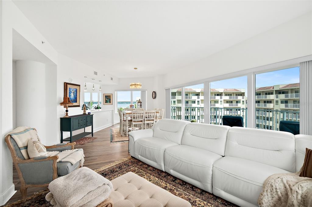 A living and dining area features white leather seating, wood flooring, and large balcony windows — 2 OCEANS WEST BOULEVARD UNIT 606, DAYTONA BEACH SHORES, FL