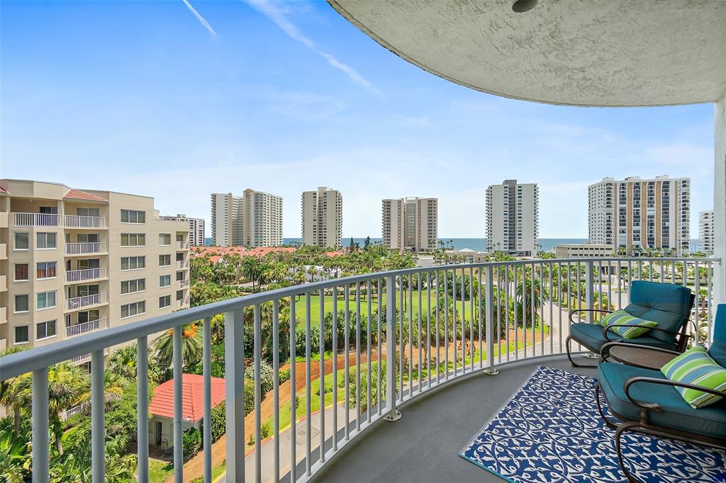 A balcony with two chairs and a rug overlooks a golf course and distant ocean — 2 OCEANS WEST BOULEVARD UNIT 606, DAYTONA BEACH SHORES, FL