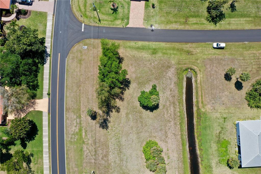 An aerial view shows a vacant corner lot with trees, grass, and a drainage ditch — 17175 CAPE HORN BOULEVARD, PUNTA GORDA, FL