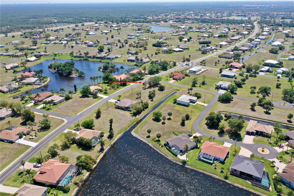 An aerial view shows a suburban neighborhood with houses, a large pond, and paved roads — 17175 CAPE HORN BOULEVARD, PUNTA GORDA, FL