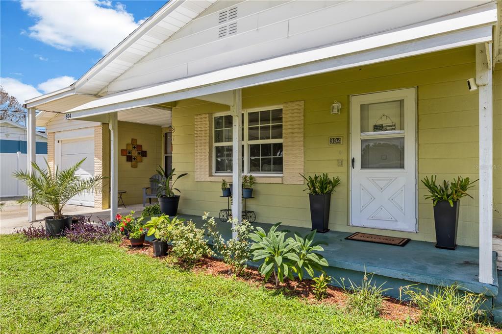 A light green house exterior features a covered front porch with potted plants and landscaping — 304 W LAKE AVENUE, AUBURNDALE, FL