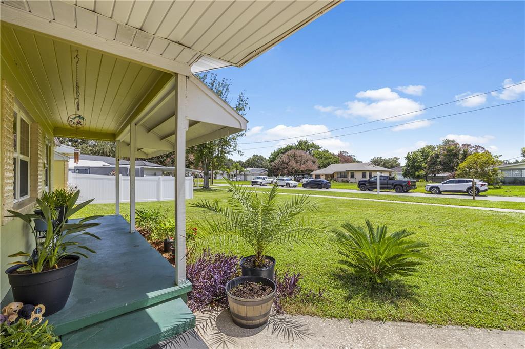A covered front porch with potted plants overlooks a grassy front yard and suburban street — 304 W LAKE AVENUE, AUBURNDALE, FL