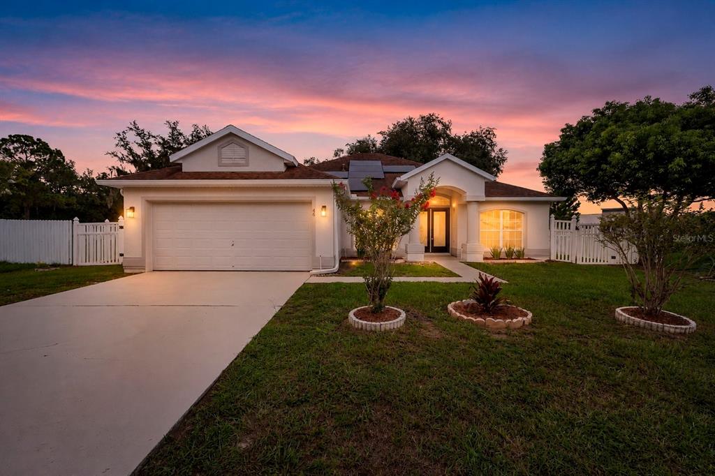 A single-story suburban house with a two-car garage and a white fence at sunset — 46 CORDONA DRIVE, KISSIMMEE, FL