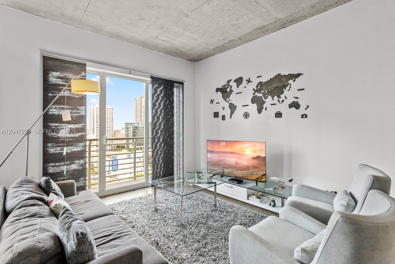 A modern living room features a gray sofa, two armchairs, a glass coffee table, and a wall-mounted world map — 133 NE 2nd Ave # 1815, Miami FL 33132, MIAMI, FL