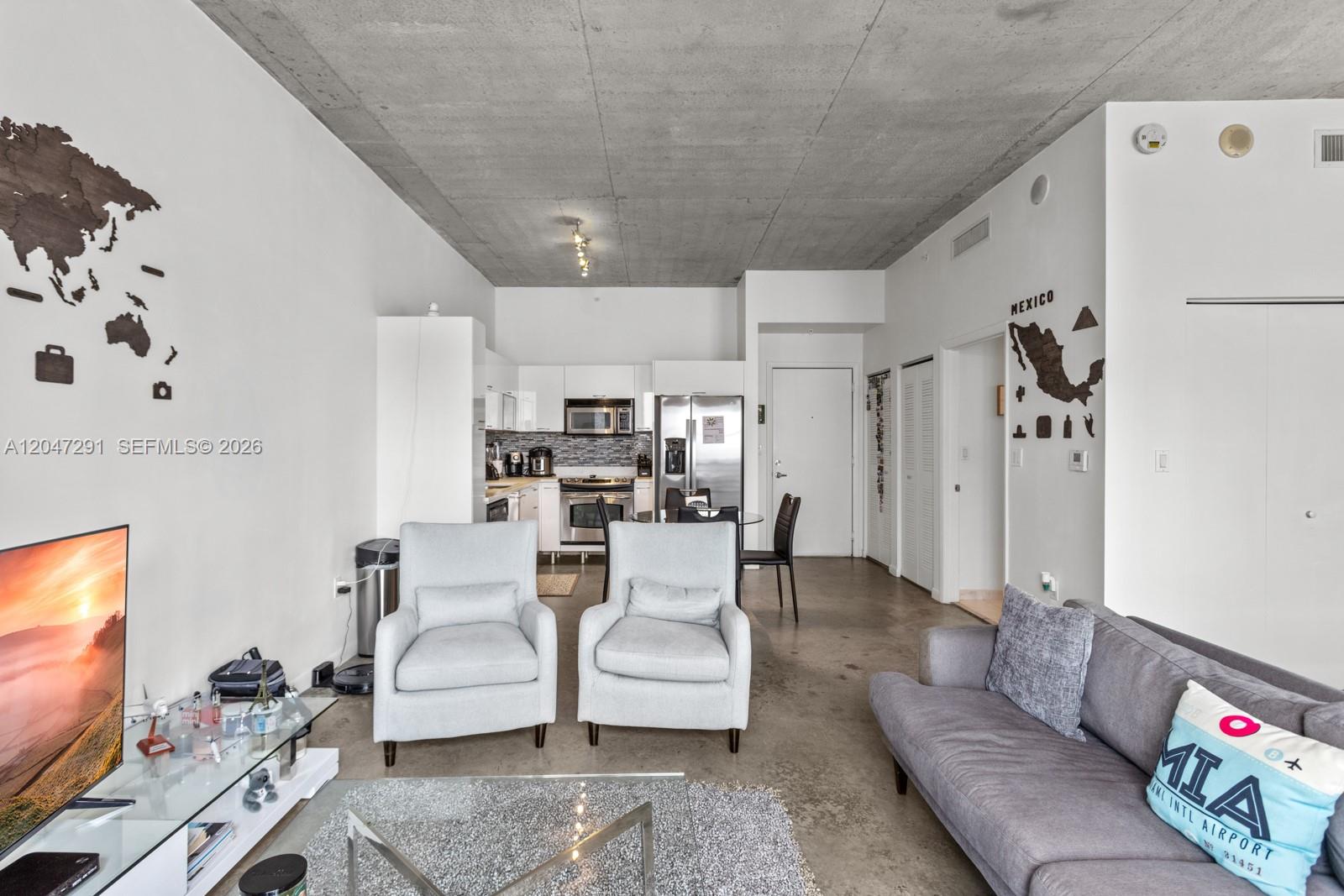 An open-concept living room and kitchen feature concrete ceilings, polished floors, and modern furniture — 133 NE 2nd Ave # 1815, Miami FL 33132, MIAMI, FL