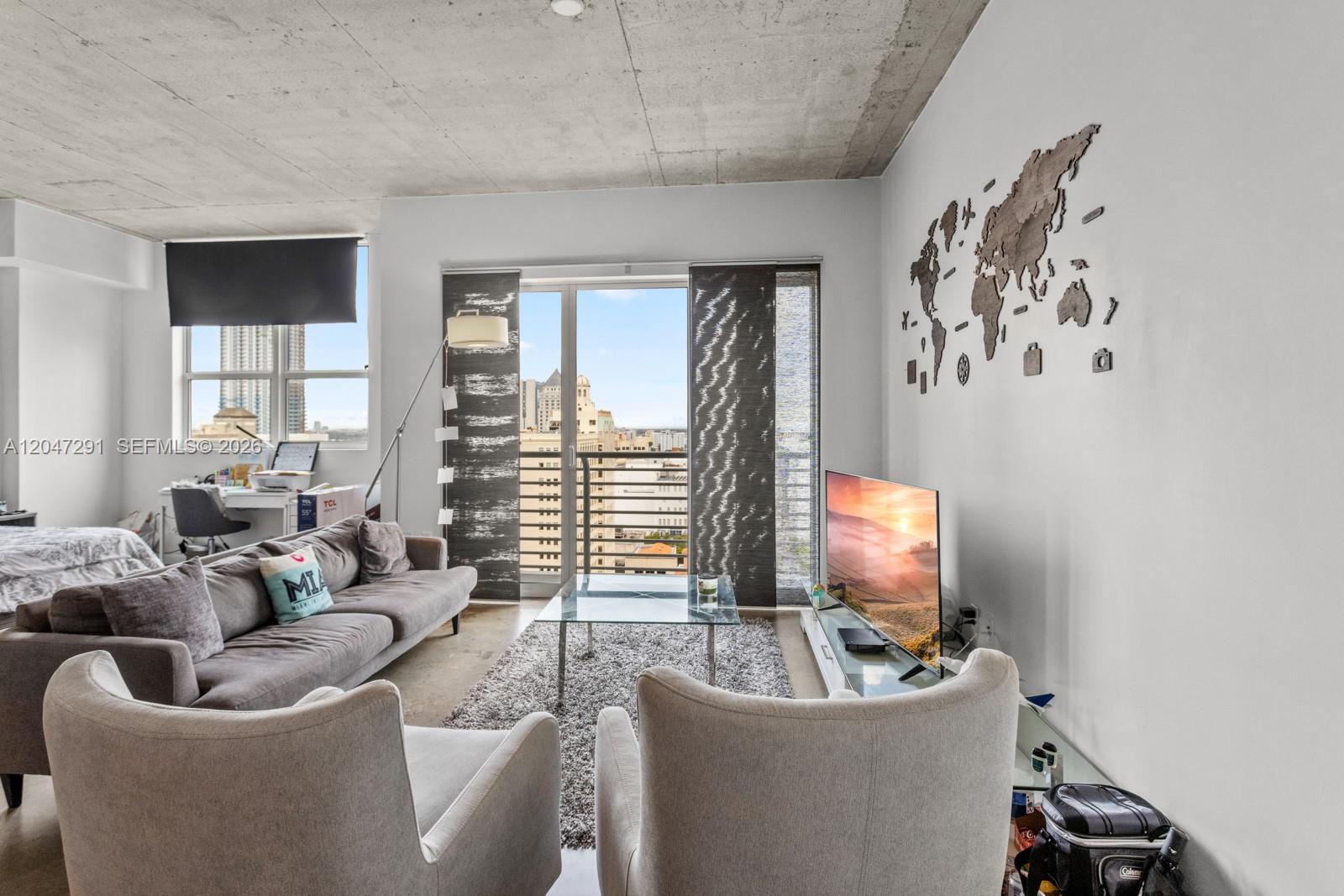 A living room features a concrete ceiling, gray sofa, two armchairs, and a world map wall — 133 NE 2nd Ave # 1815, Miami FL 33132, MIAMI, FL