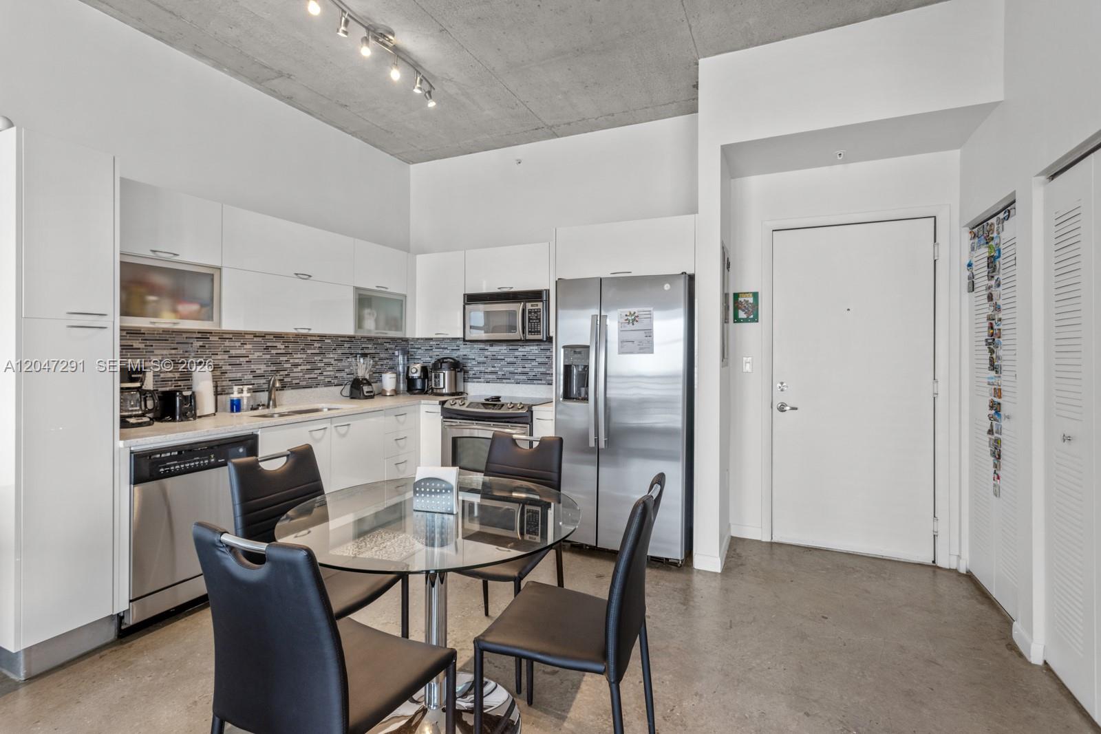 A modern kitchen features white cabinetry, stainless steel appliances, and a glass dining table — 133 NE 2nd Ave # 1815, Miami FL 33132, MIAMI, FL