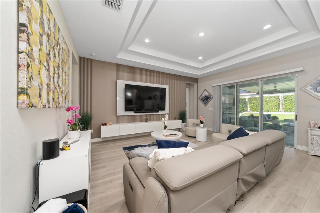 A modern living room features a wall-mounted television, a floating console, and a sectional sofa — 5128 BREEZY ACRES STREET, WINTER GARDEN, FL