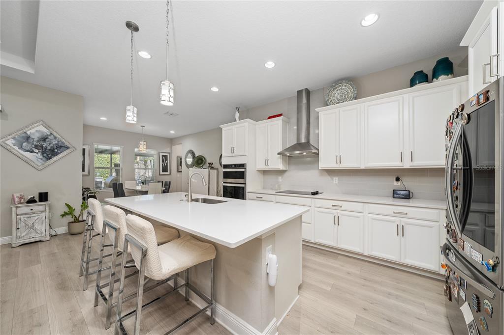 A modern kitchen features white cabinetry, a large quartz island with bar seating, and stainless appliances — 5128 BREEZY ACRES STREET, WINTER GARDEN, FL
