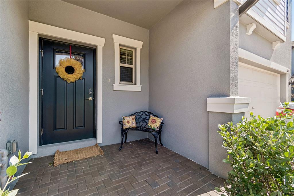 A front porch with a dark door, a small window, a metal bench, and brick pavers — 21851 LYONIA LANE, LAND O LAKES, FL