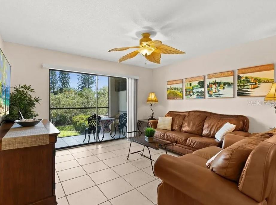 A living room features brown leather sofas, tile flooring, a ceiling fan, and a sliding door — 1669 SEASCAPE CIRCLE UNIT 1669, TARPON SPRINGS, FL