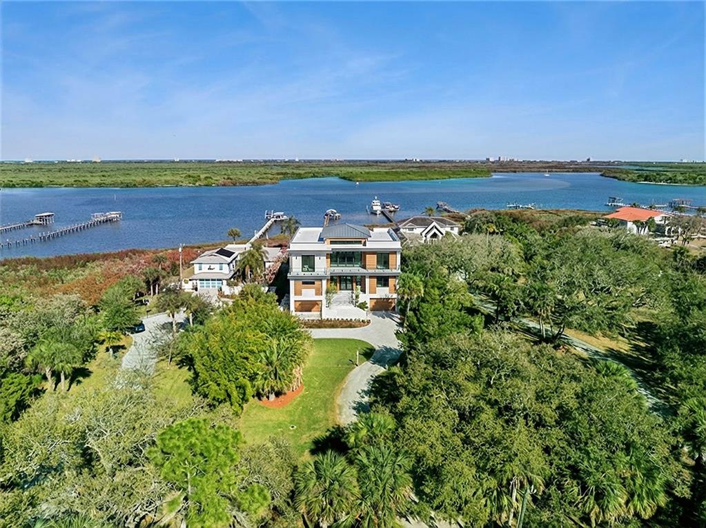 An aerial view shows a modern three-story house surrounded by trees near a waterfront — 1703 S RIVERSIDE DRIVE, NEW SMYRNA BEACH, FL