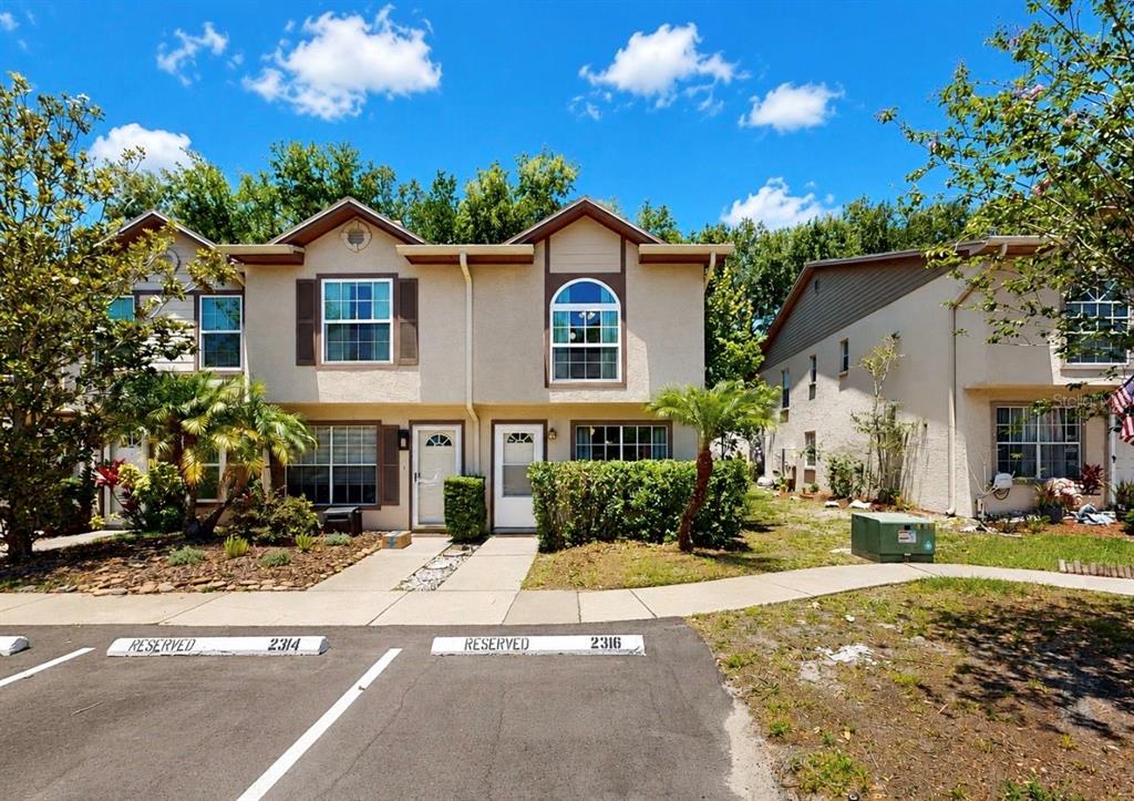 A two-story townhouse exterior with tan stucco siding, brown trim, and reserved parking spaces — 2316 FLETCHERS POINT CIRCLE, TAMPA, FL