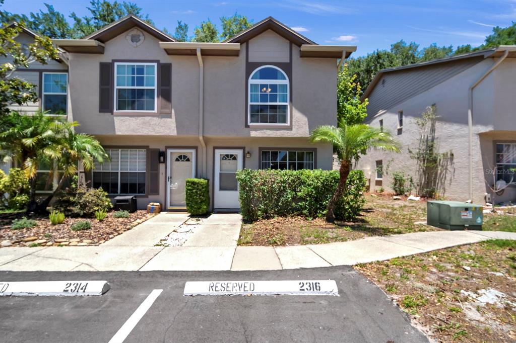 A two-story townhouse exterior features beige stucco siding, brown trim, and reserved parking spaces — 2316 FLETCHERS POINT CIRCLE, TAMPA, FL
