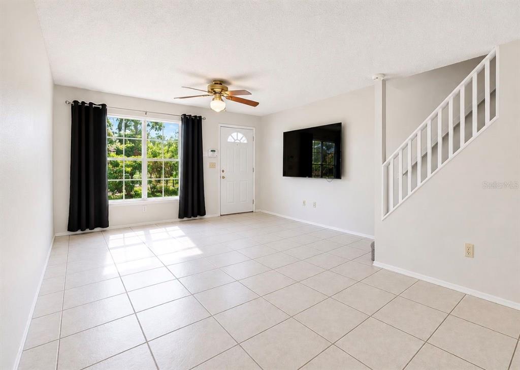 A living room with tile floors, a ceiling fan, a wall-mounted television, and a staircase — 2316 FLETCHERS POINT CIRCLE, TAMPA, FL