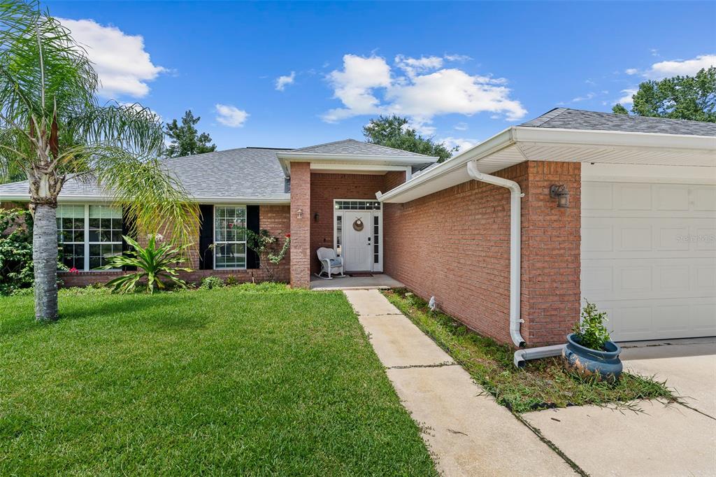A single-story brick house features a white front door, a concrete walkway, and a garage — 23 POWDER HILL LANE, PALM COAST, FL