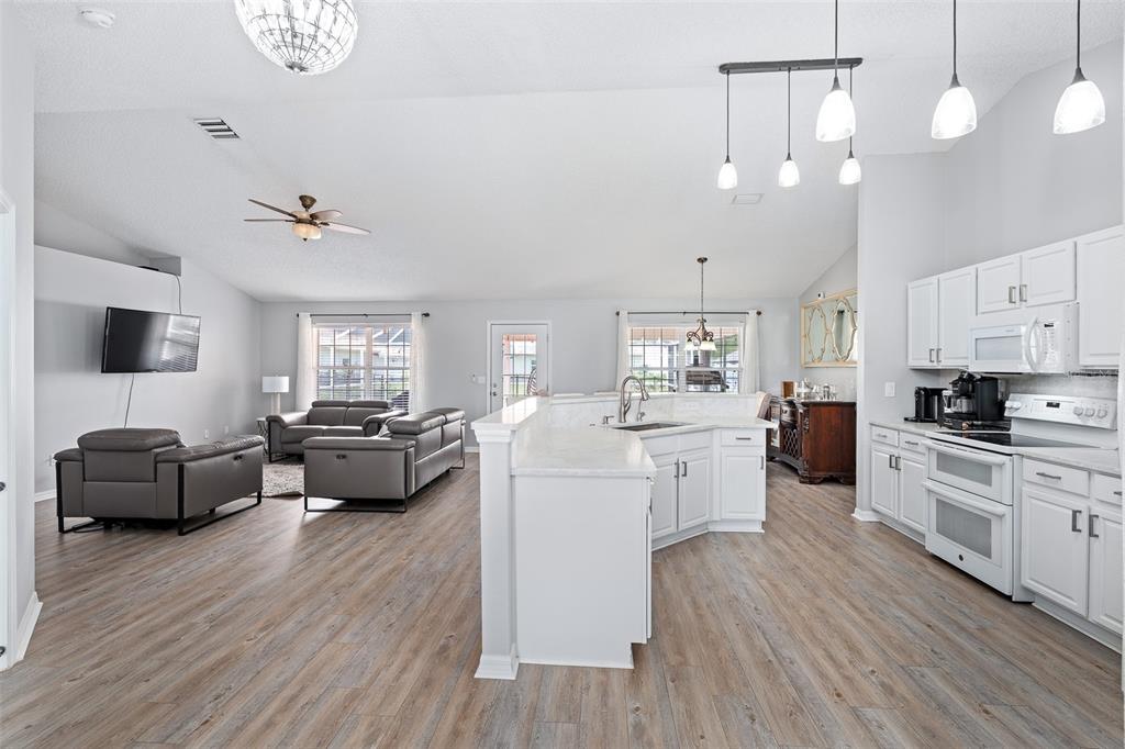 An open-concept living room and kitchen with white cabinetry, gray furniture, and wood-look flooring — 23 POWDER HILL LANE, PALM COAST, FL