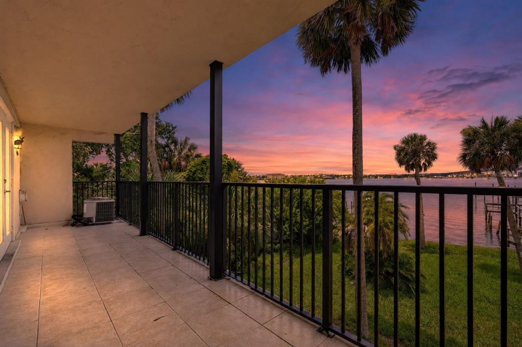A tiled balcony with a black railing overlooks a grassy yard, palm trees, and water — 900 S PENINSULA DRIVE UNIT 214, DAYTONA BEACH, FL