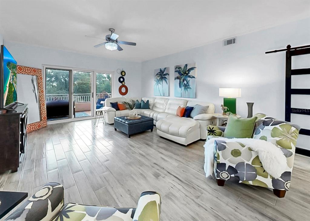 A living room features a white sectional sofa, patterned armchairs, and light wood-look tile flooring — 12033 GANDY BOULEVARD N UNIT 133, ST PETERSBURG, FL