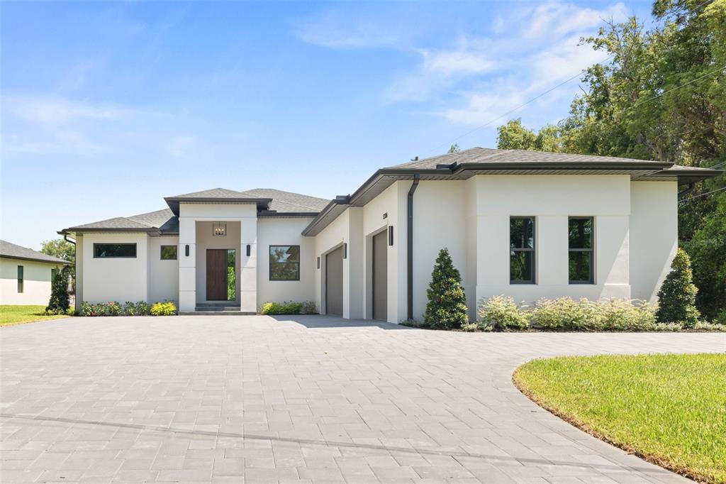 A modern, single-story house with white stucco walls, a dark roof, and a paved driveway — 1336 HAYS ROAD, TARPON SPRINGS, FL