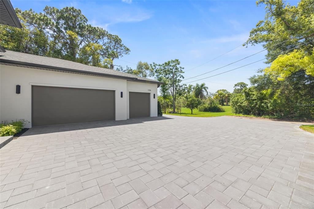 A paved driveway leads to a three-car garage on the side of a white house — 1336 HAYS ROAD, TARPON SPRINGS, FL