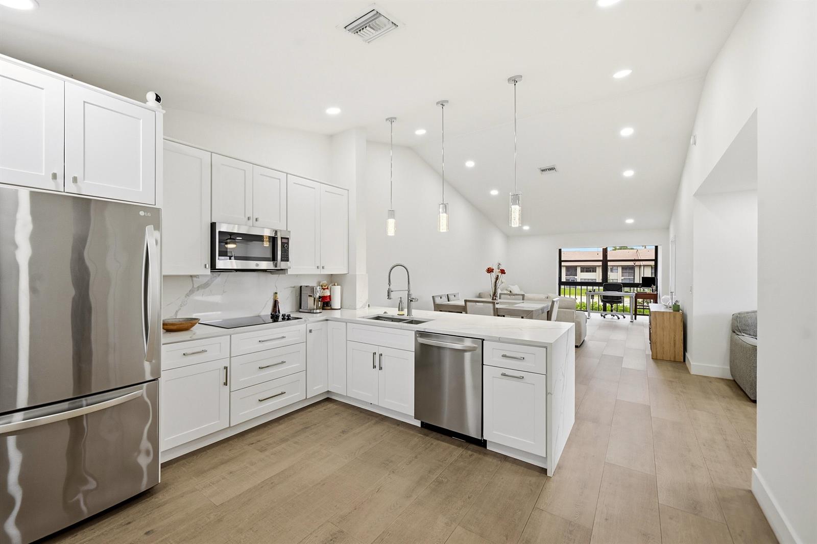 A modern kitchen with white cabinets, stainless steel appliances, and quartz countertops overlooks a living area — 4699 E Lucerne Lakes Boulevard # 206, Lake Worth FL 33467, LAKE WORTH, FL