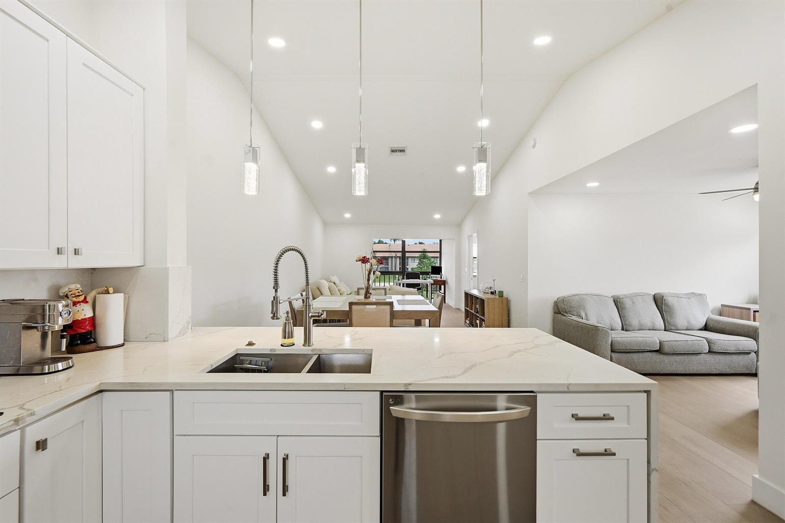 A modern kitchen with white cabinets and quartz countertops overlooks an open-concept living area — 4699 E Lucerne Lakes Boulevard # 206, Lake Worth FL 33467, LAKE WORTH, FL
