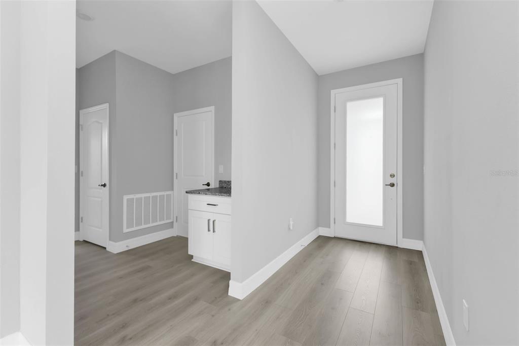 A hallway with light gray walls, wood-look flooring, a white door, and a small cabinet — 17022 ESPANA CIRCLE, PUNTA GORDA, FL