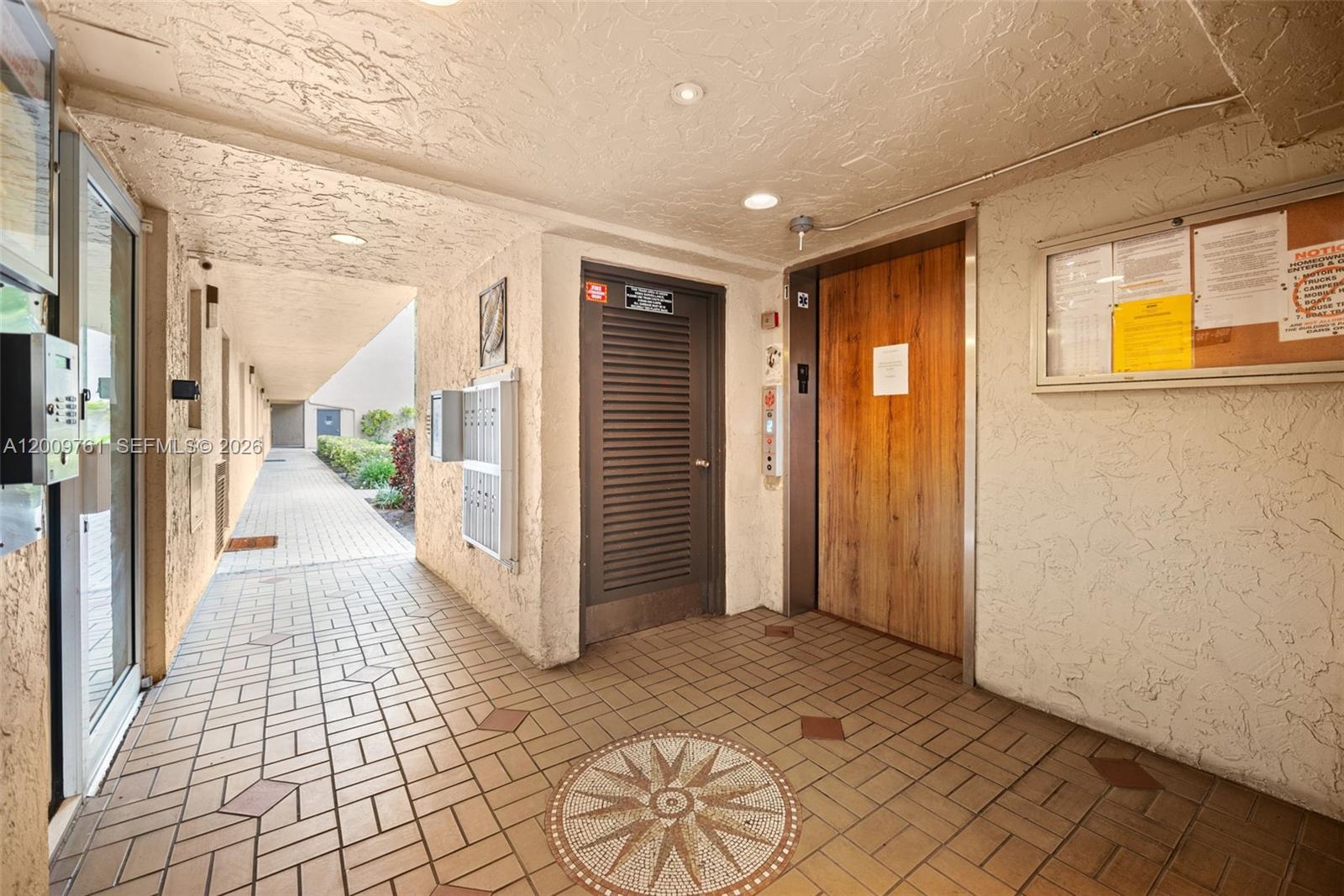 An outdoor hallway features a tiled floor, a wooden elevator door, and a louvered utility door — 3300 W Rolling Hills Cir # 510, Davie FL 33328, DAVIE, FL
