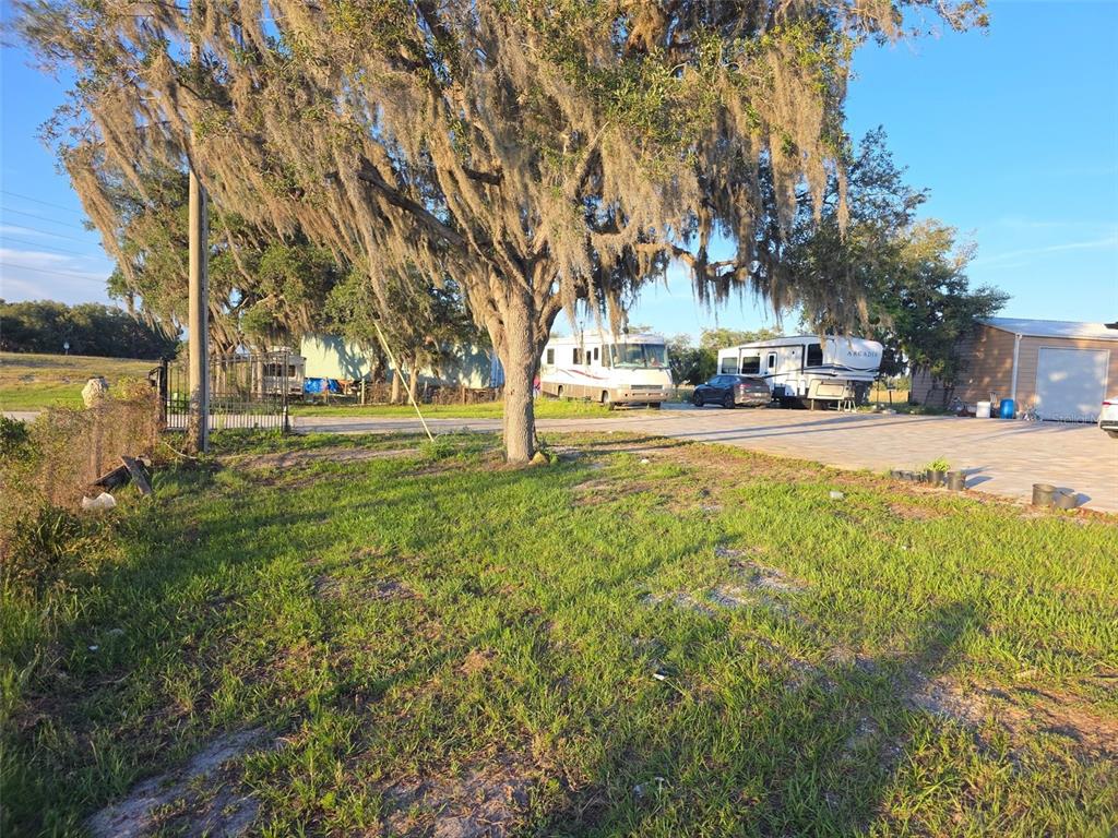 A grassy lot features a large moss-covered tree, a paved driveway, and several parked RVs — 3620 COUNTY ROAD 64 E, AVON PARK, FL