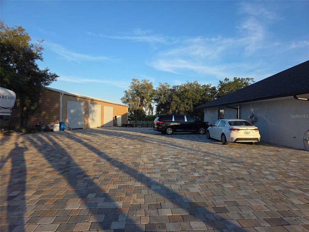A paved driveway sits between a house and a detached garage under a blue sky — 3620 COUNTY ROAD 64 E, AVON PARK, FL