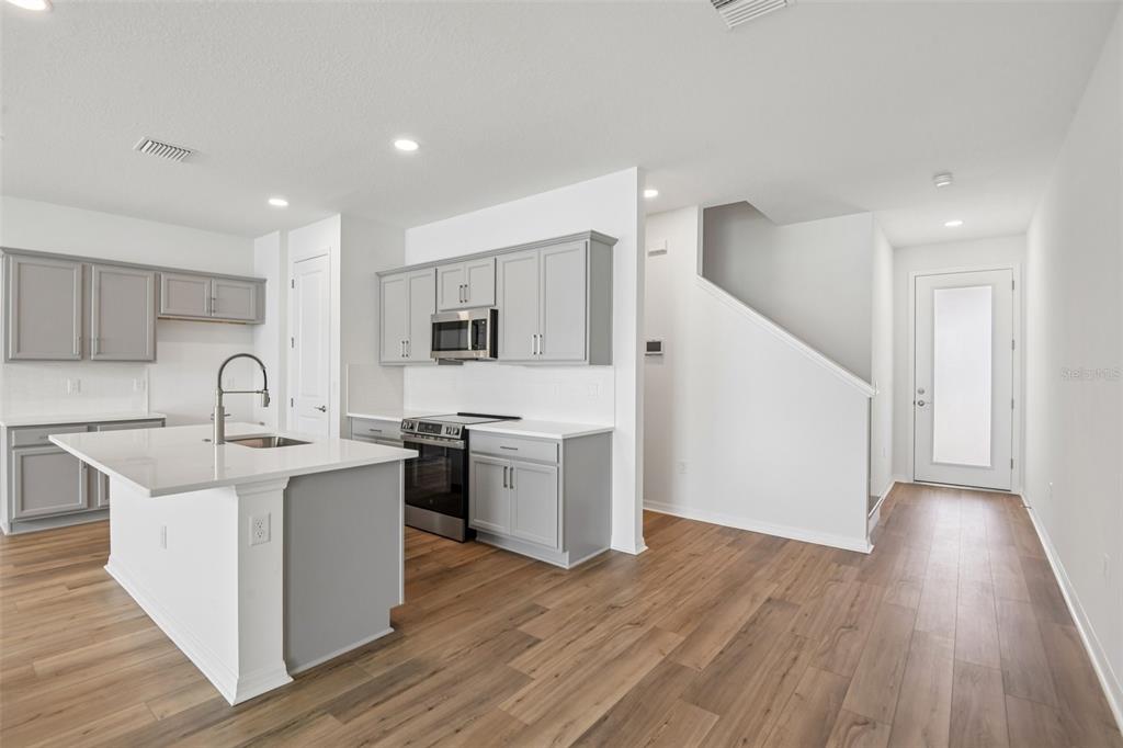A modern kitchen features gray cabinets, white countertops, a center island, and wood-look flooring — 31542 AZURE BEACH DRIVE, SAN ANTONIO, FL