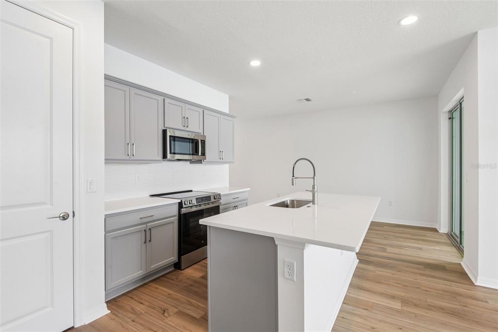 A kitchen with gray cabinetry, white countertops, a center island, and light wood-look flooring — 31542 AZURE BEACH DRIVE, SAN ANTONIO, FL