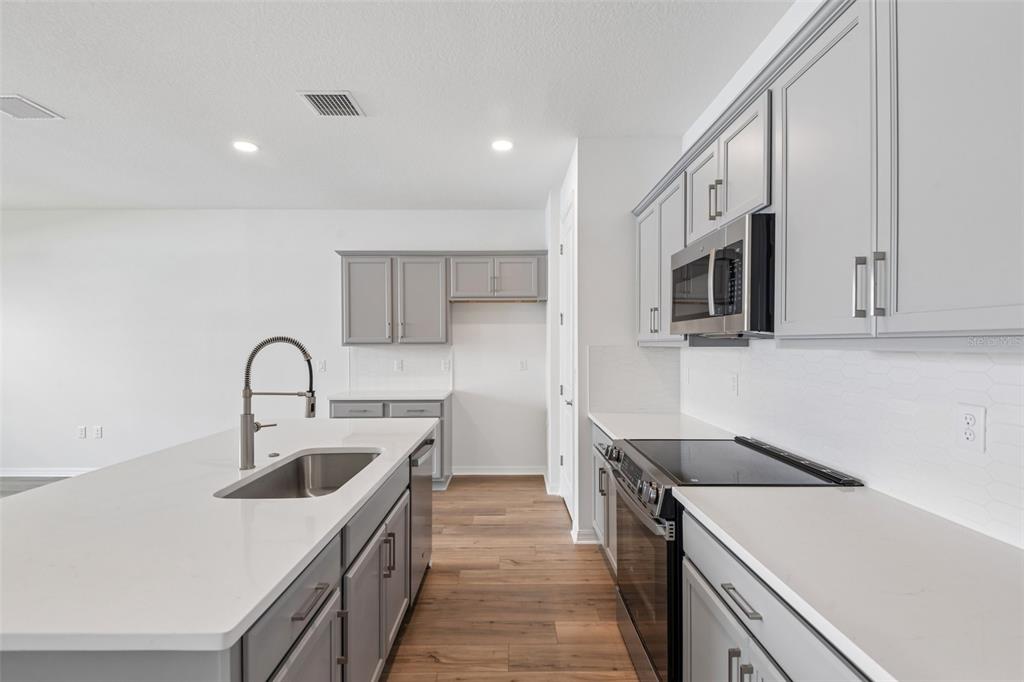 A modern kitchen features gray cabinets, white countertops, a kitchen island, and stainless steel appliances — 31542 AZURE BEACH DRIVE, SAN ANTONIO, FL
