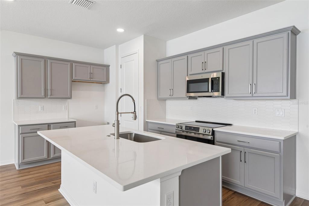 A modern kitchen features gray cabinets, white countertops, a central island, and stainless steel appliances — 31542 AZURE BEACH DRIVE, SAN ANTONIO, FL