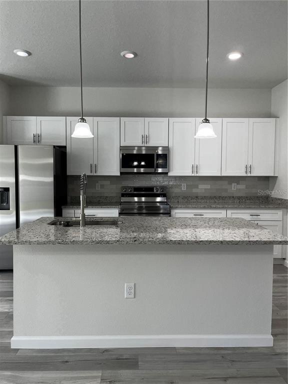 A kitchen features a granite-topped island, white cabinetry, stainless steel appliances, and pendant lighting — 5312 SW 162ND PLACE ROAD, OCALA, FL