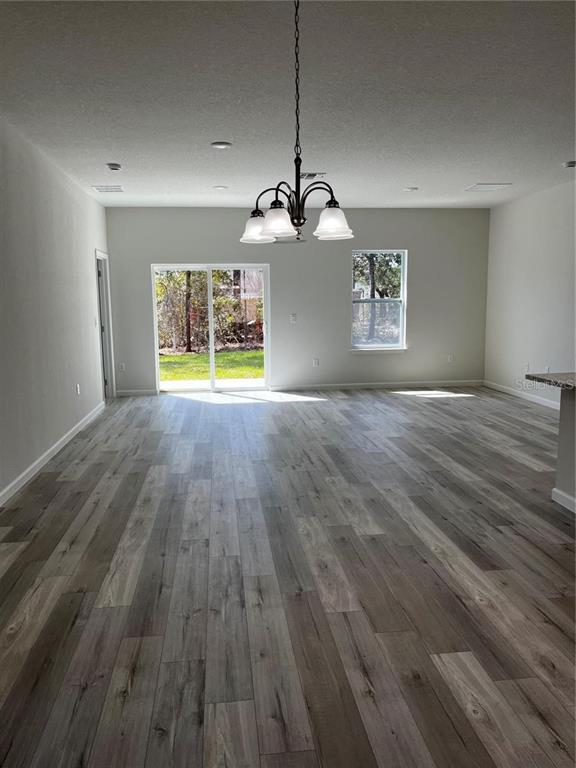 An open-concept room features light gray wood-look flooring, a chandelier, and a sliding glass door — 5312 SW 162ND PLACE ROAD, OCALA, FL