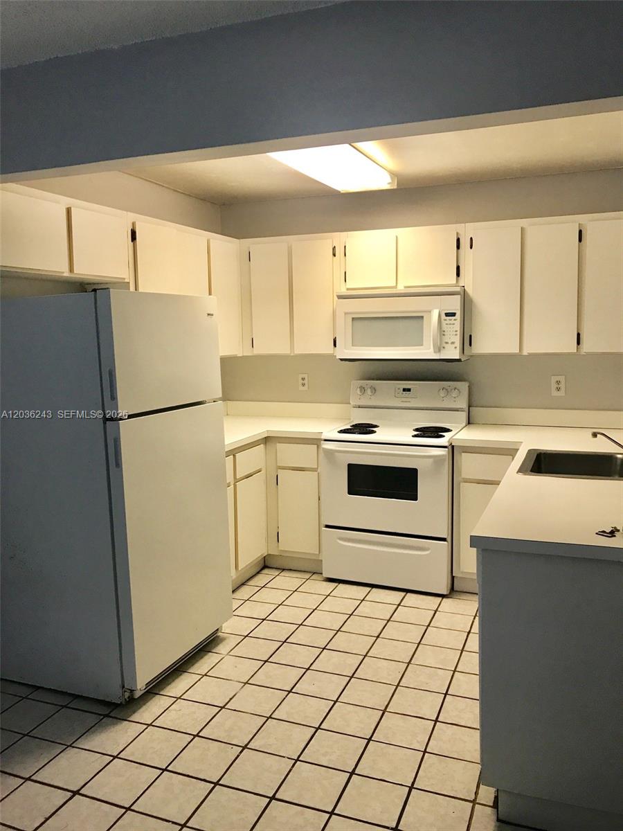 A kitchen features white cabinets, white appliances, and light-colored tile flooring — 9810 Hammocks Blvd # 202, Miami FL 33196, MIAMI, FL