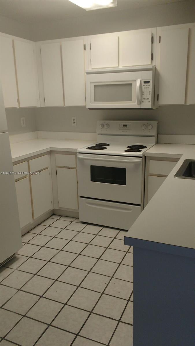 A kitchen features white cabinets, white appliances, a white countertop, and tiled flooring — 9810 Hammocks Blvd # 202, Miami FL 33196, MIAMI, FL