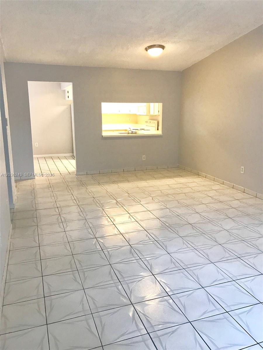 An empty room features light-colored tile flooring, gray walls, and a kitchen pass-through window — 9810 Hammocks Blvd # 202, Miami FL 33196, MIAMI, FL